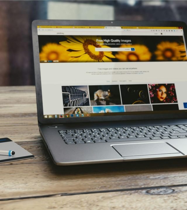 Laptop with open webpage on wooden desk, accompanied by tablet and pen, representing digital work setup.